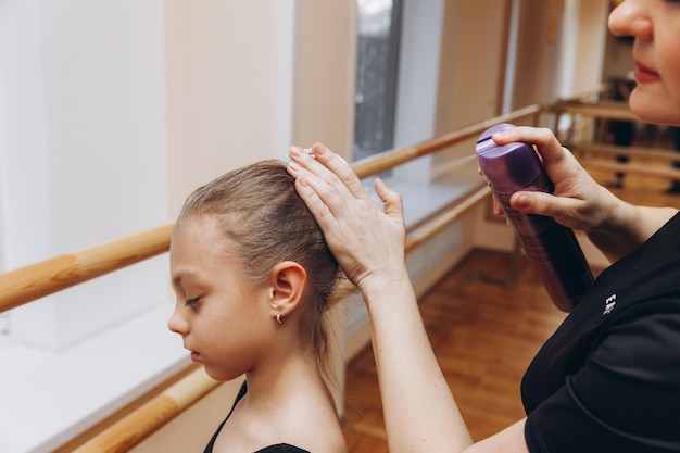 女の子はヘアスプレーを使用しています。女性がワニスの入ったスプレーボトルを持って頭にスプレーします。