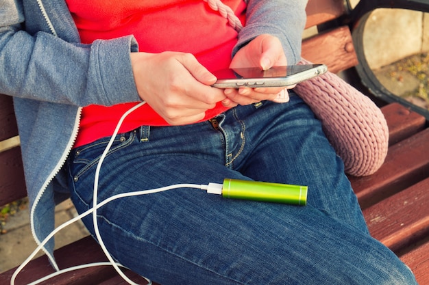 A girl uses a smartphone outdoors while charging from an external power bank