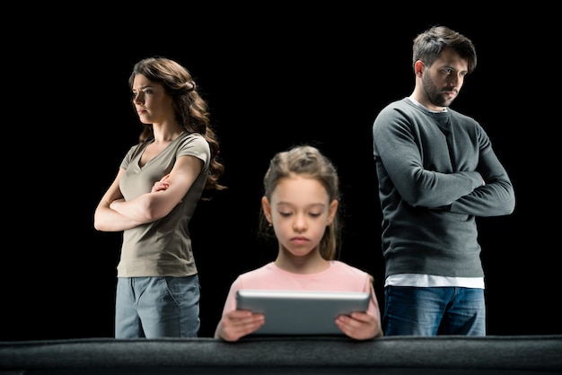 Girl using digital tablet while parents standing with crossed arms on black