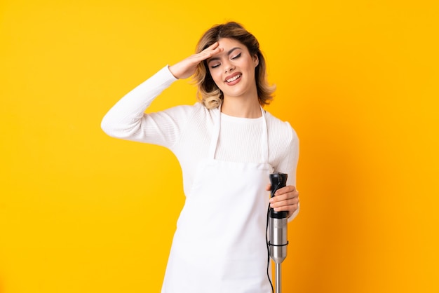 Girl using hand blender isolated on yellow looking far away with hand to look something