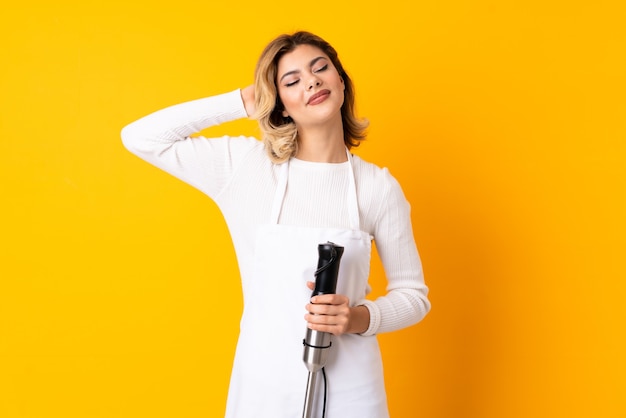 Girl using hand blender isolated on yellow wall laughing