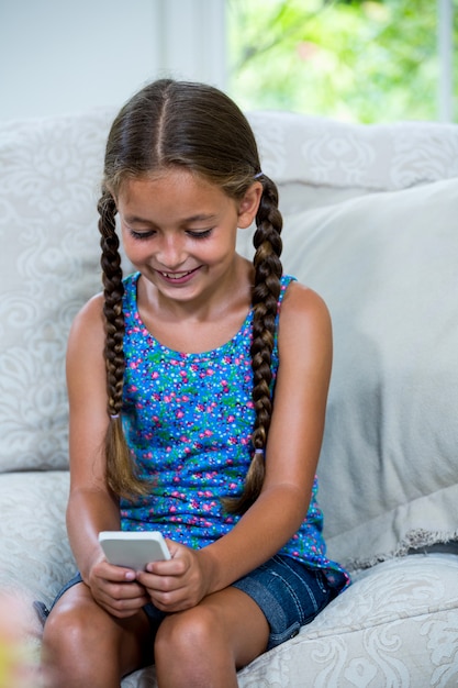 Girl using mobile phone while sitting on sofa at home