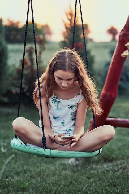 Photo girl using mobile phone while sitting on swing