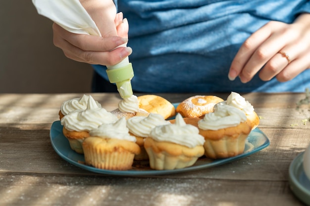 a girl using a pastry bag decorates cupcakes with cream