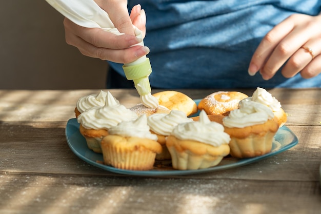 a girl using a pastry bag decorates cupcakes with cream