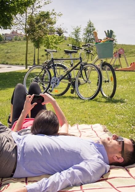 Photo girl using smartphone lying over man on the park