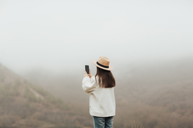 視点の女の子が霧の山の写真を撮っています。