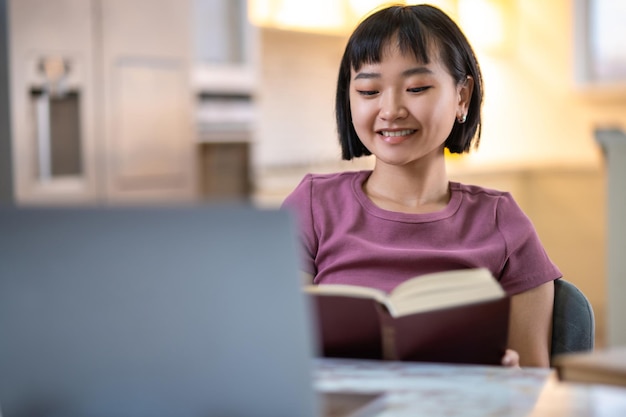 A girl in violet tshirt sitting at the laptop and looking happy