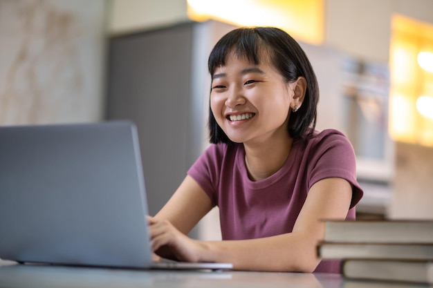 A girl in violet tshirt sitting at the laptop and looking happy