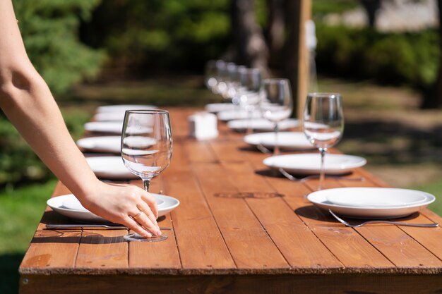 Girl the waiter in a summer cafe under the open sky arranges the dishes on a wooden banquet table.