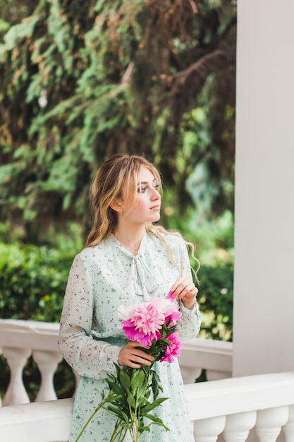 Girl waits for date holding bouquet of peonies