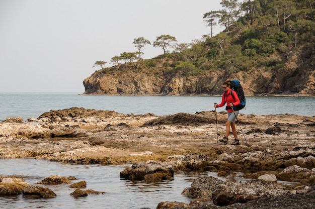 Girl walking on the rocks on the sea with hiking backpack