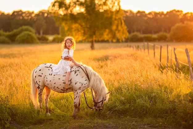 Girl walking at sunset in a field with a horse