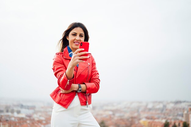 Girl walking and texting on red smartphone with city in background