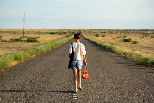 Una ragazza cammina lungo una strada vuota nella steppa ha un ukulele e uno zaino strada aperta
