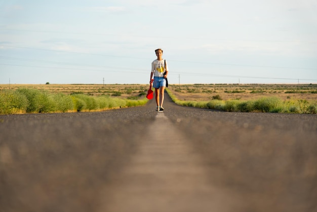 A girl walks along an empty road in the steppe She has a ukulele and a backpack Open road