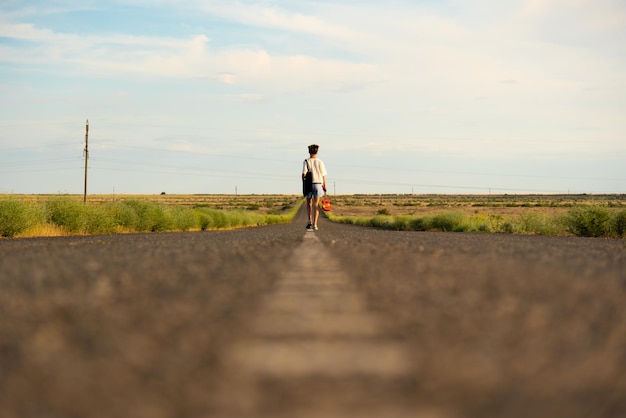 A girl walks along an empty road in the steppe. she has a\
ukulele in her hands and a backpack on her shoulders. it\'s summer\
and warm outside. open road.
