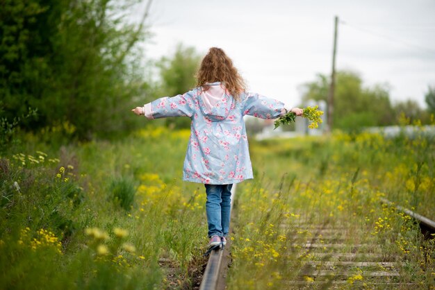 A girl walks along the grassy railroad tracks The victory of nature over the vitality of man