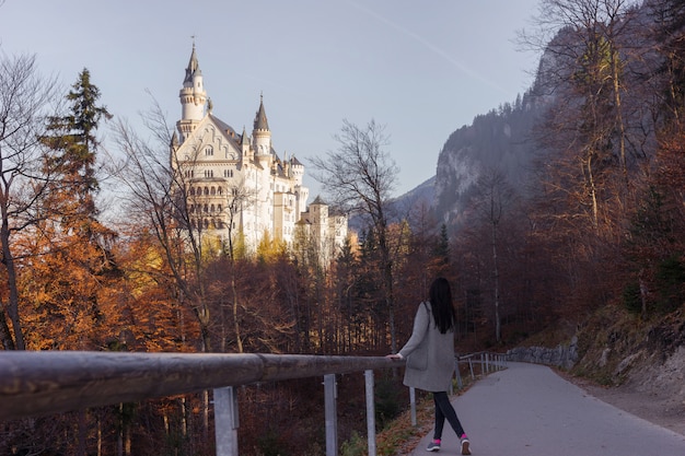 Photo the girl walks along the path in the autumn forest to a very beautiful castle neuschwanstein, germany.