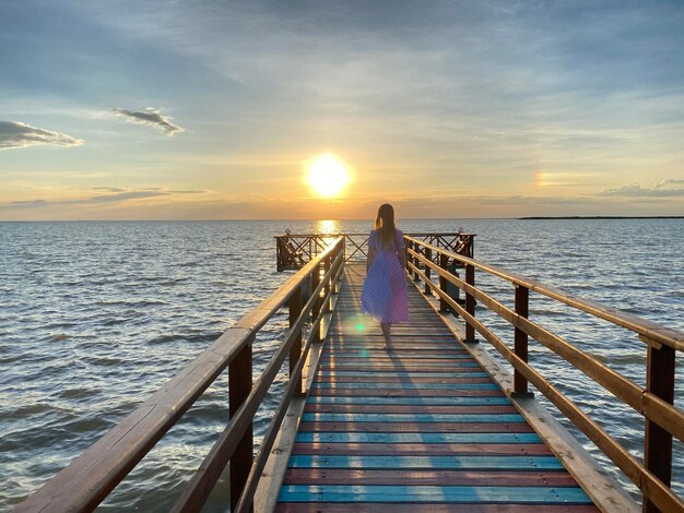 A girl walks on a pier at sunset