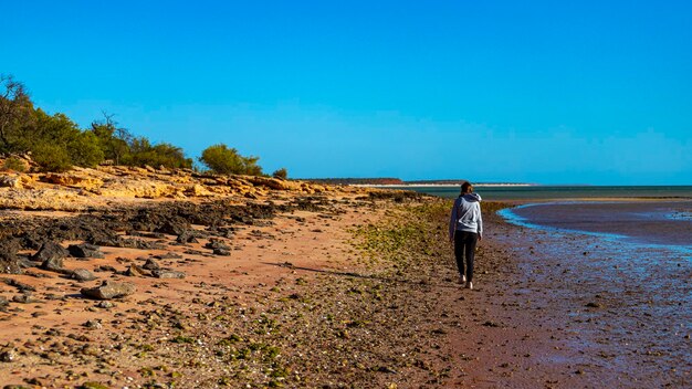 girl walks on red sand beach with red cliffs in the background, terra rosa in australia