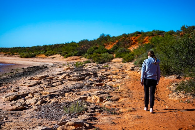 девушка ходит по пляжу с красным песком на фоне красных скал, терра-роза в австралии