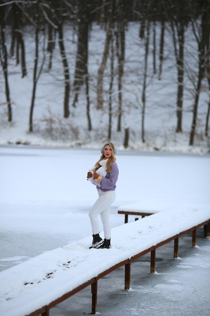 A girl walks on a small bridge on the lake Winter beauty is all around Warm fashionable clothes
