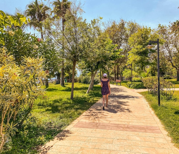 The girl walks through the park with large green trees tropical green island walk on a hot day