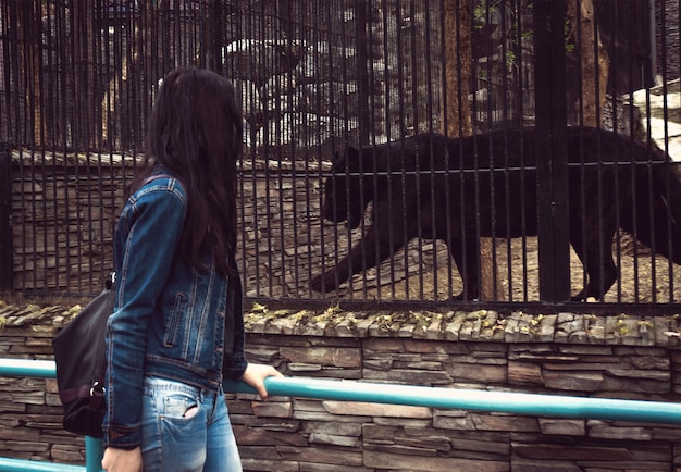 The girl walks through the zoo and looking at animals in cages. Black Jaguar in a cage.