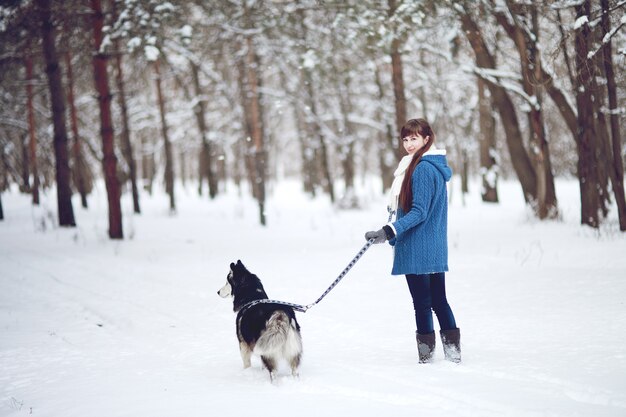 少女は冬の雪に覆われた森で犬のシベリアンハスキーと一緒に歩く