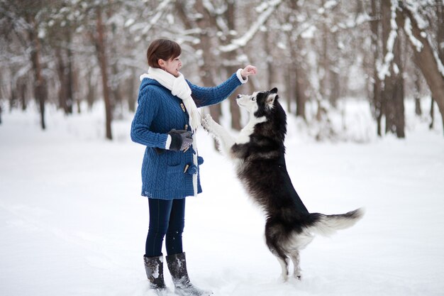 The girl walks with dog siberian husky in a winter snowy forest.