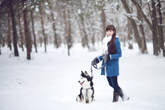 The girl walks with dog siberian husky in a winter snowy forest.