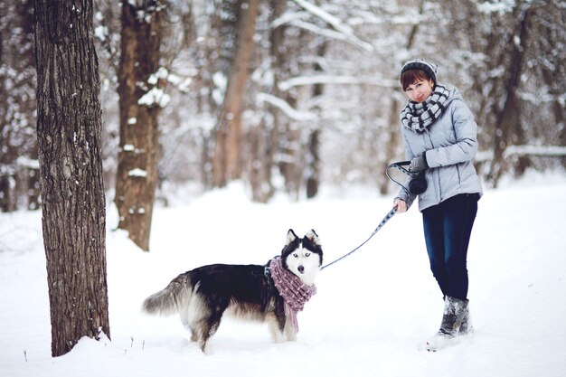 The girl walks with dog siberian husky in a winter snowy forest.