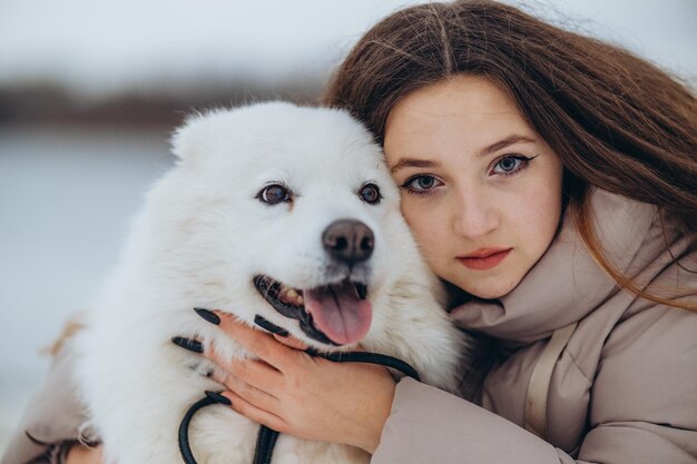 A girl walks with her beloved pet Samoyed in winter on the shore of a lake in the park Walking the dog in winter