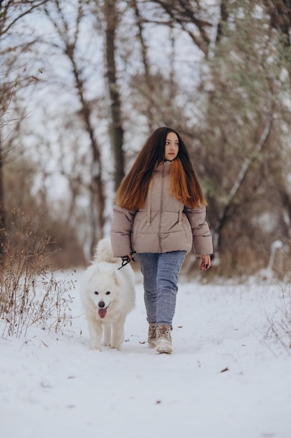 A girl walks with her beloved pet Samoyed in winter on the shore of a lake in the park Walking the dog in winter