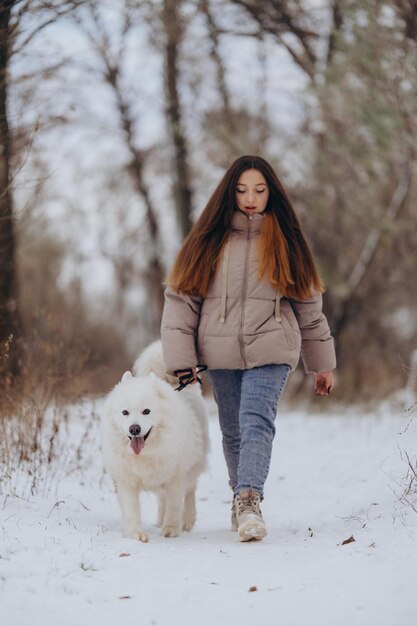 A girl walks with her beloved pet Samoyed in winter on the shore of a lake in the park Walking the dog in winter