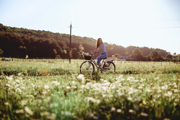 La ragazza cammina con un cucciolo in un campo in una bicicletta nella parte posteriore della luce solare