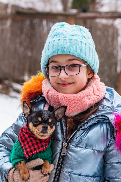 Girl in warm clothing and gray glasses. Teenage girl in a blue hat. Girl with chihuahua in her arms