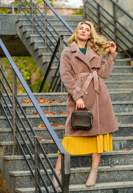 女の子の暖かいコートは都会の階段の背景に立つ 快適でかわいい秋の服装を作成する 秋の服装 女性はスタイリッシュな服装を着て財布を運ぶ モダンで暖かくスタイリッシュなエコファーのアウター