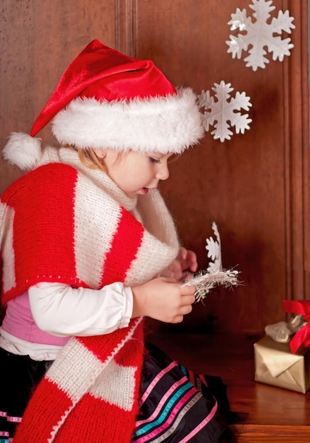 A girl in a warm red scarf and a santa claus hat examines paper snowflakes The child rejoices in winter New Year cartoons and the holiday of Christmas