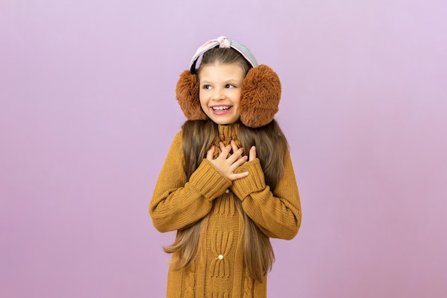 A girl in a warm sweater and fur headphones put her hands to\
her heart on an isolated background