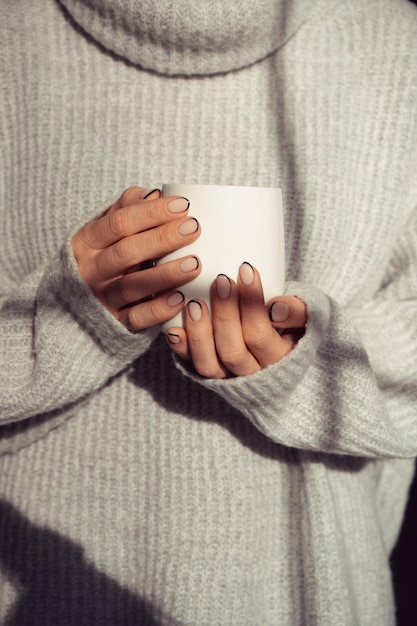 A girl in a warm sweater holding a mug in her hands