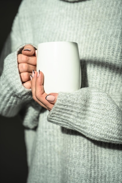 A girl in a warm sweater holding a mug in her hands