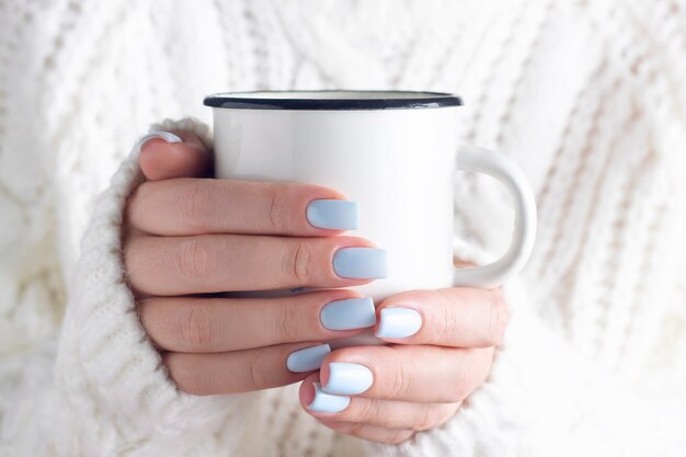 Una ragazza con un maglione lavorato a maglia bianco caldo tiene una tazza con un primo piano di una bevanda calda.