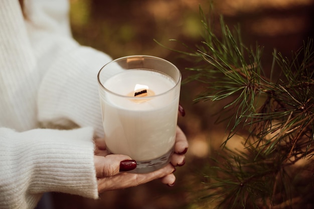 Girl in warm white sweater holding candle in her hands near a spruce branch