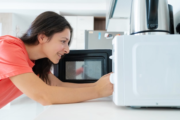 The girl warms food in the microwave. A quick snack.