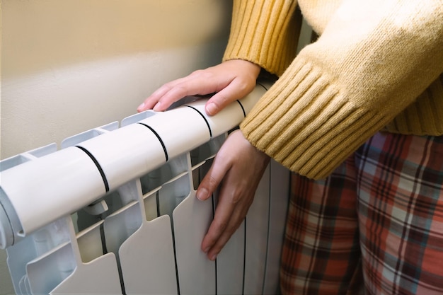 The girl warms her hands at the battery or radiator. The cold season