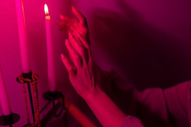A girl warms her hands by a burning candle women\'s hands\
closeup pink purple colors