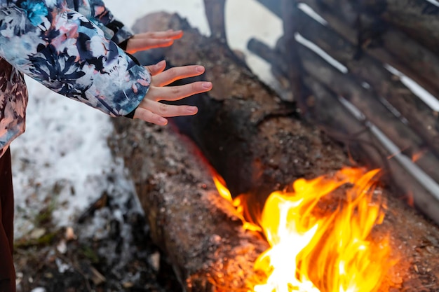 The girl warms her hands over the fire. Burning logs in the snow.