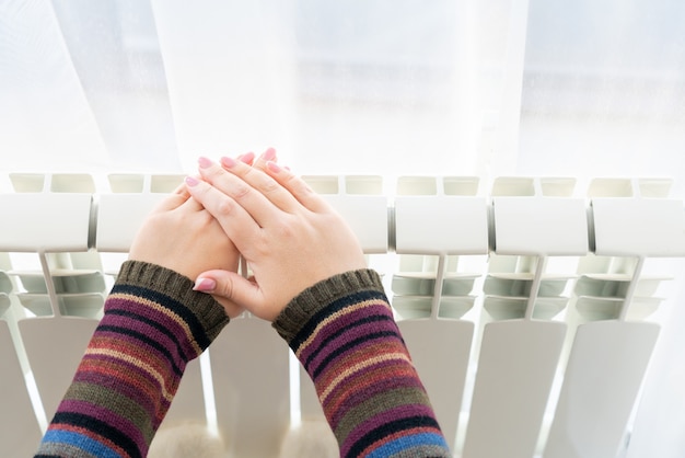 Photo girl warms up the frozen hands above hot radiator, close up view